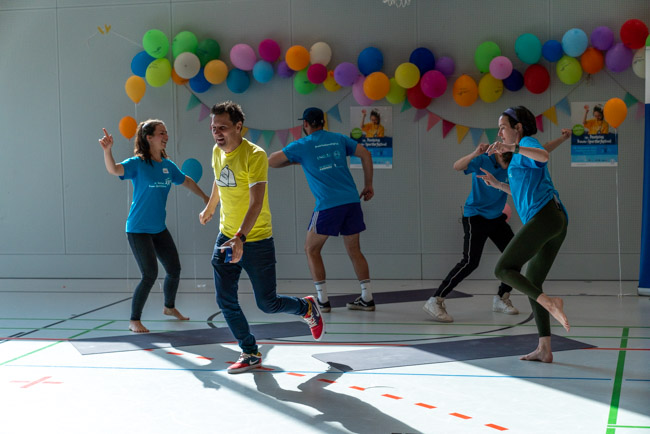 Foto: Moderator André Gatzke und Trainer tanzen mit großer Freude in der Sporthalle.