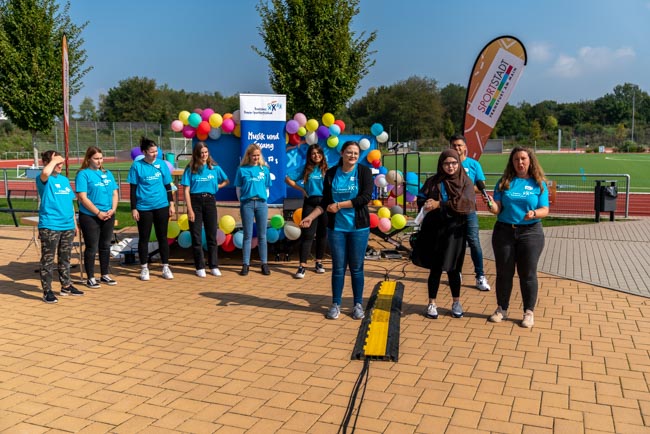 Foto: Gruppe von Helfenden in blauen Shirts steht vor bunten Ballons im Freien.